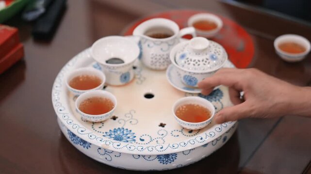Hand serving tea from traditional ceramic tea set on wooden table
