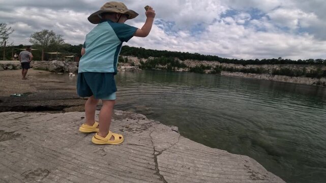 Boy throwing stones into a lake from a rocky shore