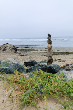 Stacked stones on the rocky shore of Pacific Beach Coast at Tourmaline Surfing Park in San Diego, California, under an overcast sky