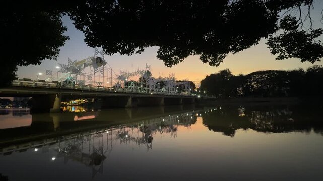 Illuminated Nawarat bridge reflecting on river at dusk in Chiang Mai