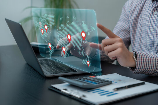 Business person using a laptop and interacting with a transparent holographic display showing a map with red location pins for global logistics and tracking