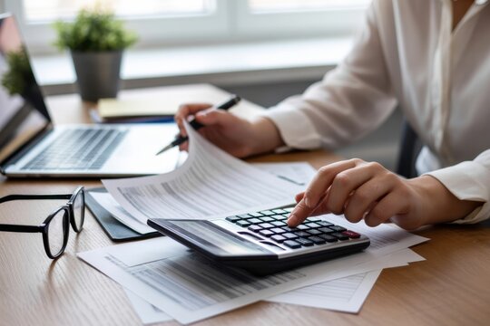Business working with financial documents, using a calculator and laptop at a desk, analyzing data reports and tax information in a modern office setting