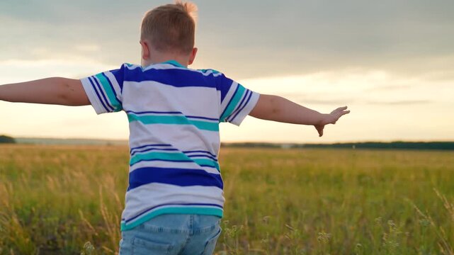 Child boy runs through green grass in sun, Dream kid. Joyful little boy running at sunset. Kid is running across field. Childhood dream happiness concept. Happy child playing in nature. Happy family