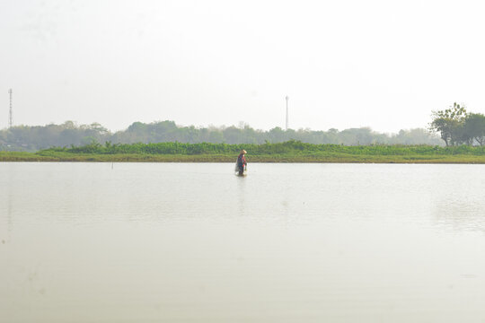 Fisherman wearing conical hat wading in shallow lake water