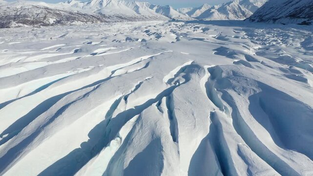 Drone Pan and Tilt Shot Rising Above Frozen Glacier Crevasses and Mountain Range