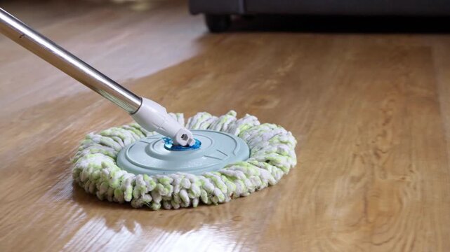 Close-up view of a wet cleaning mop sliding on a shiny wooden laminate floor. Household chore and home hygiene maintenance concept