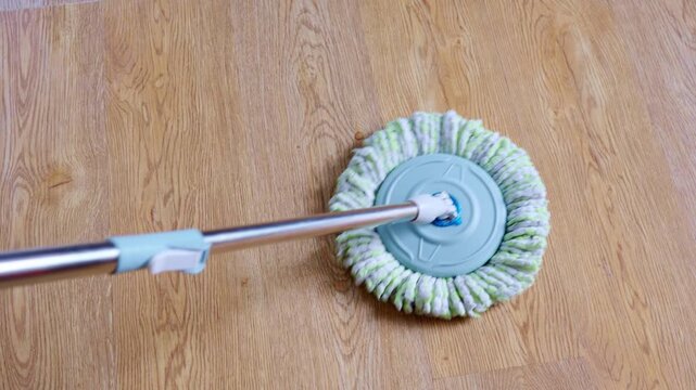 Detail shot of a spin mop featuring a microfiber head scrubbing a light brown wood-patterned floor, representing the idea of everyday household upkeep and tasks