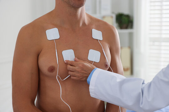 Doctor attaching ECG electrodes to patient's chest in clinic, closeup