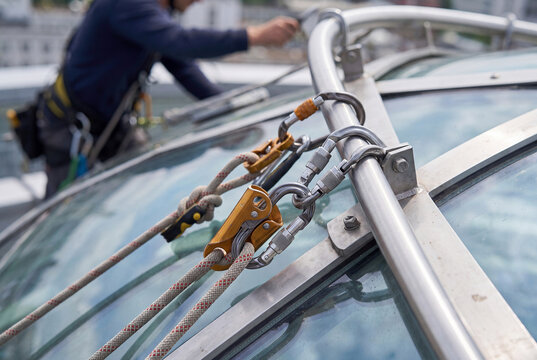 Industrial climber secures safety ropes and carabiners to a metal railing on a glass roof.