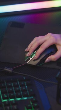 Woman hand with manicured nails operates gaming mouse on black mat positioned near illuminated keyboard. scene features vibrant RGB lighting in background and close up details of hands