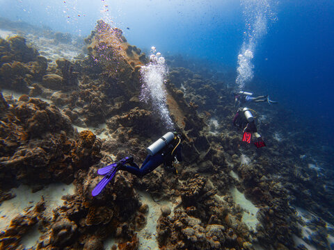 Three SCUBA divers explore a shipwreck on a coral reef near a Caribbean island