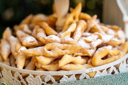 A generous mound of golden fried dough strips dusted with icing sugar rests on an ornate white cake stand, a warm invitation for a bakery menu or a home baking recipe.