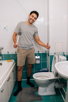 Positive guy in casual clothes doing household chores, full length portrait Concept of domestic life, hygiene, satisfaction with keeping home clean. Man posing with cleaning tool in tiled restroom