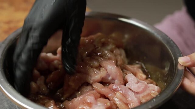 Gloved hands mixing raw sliced pork with marinade in a bowl