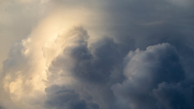 Dramatic storm clouds building up with warm golden sunlight filtering through.A powerful atmospheric photograph capturing massive cumulus storm clouds gathering in the sky. 