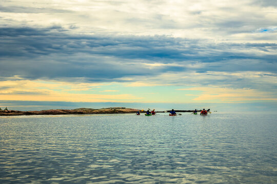Tiny line of sea kayakers dwarfed by a vast cloudy sky and open water along a granite shoreline, copy space above and below, Georgian Bay, Ontario