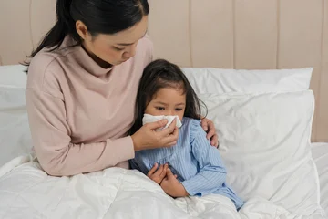 mother helping sick preschoool child girl blowing nose with tissue paper in bed © geargodz