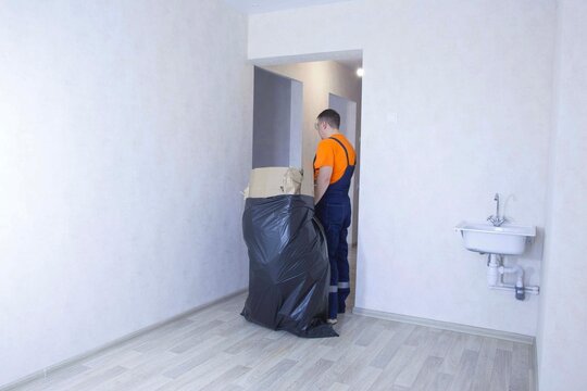 A man in a work uniform is collecting and carrying out a bag of trash from the room. Cleaning company