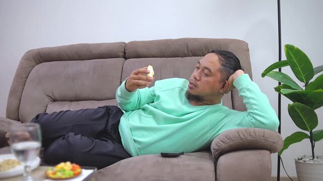 Young man Enjoy eating fresh apple while lying down and relaxing on cozy living room sofa at home