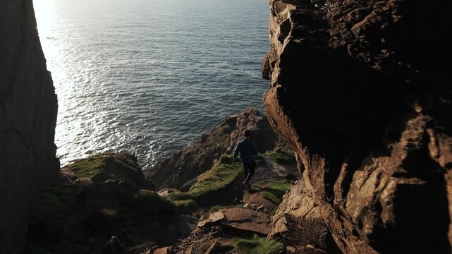 Tracking Drone Shot of Young Man Waling Between Rocks on Cliffs Above Atlantic Ocean on Coast of Ireland