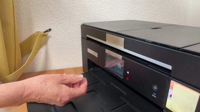 Woman's hands open a printer and press the copy button from a different perspective. She waits as the machine operates and the finished printed sheet comes out. Static shot.