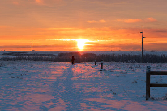 A person walking in a snowy field at sunrise