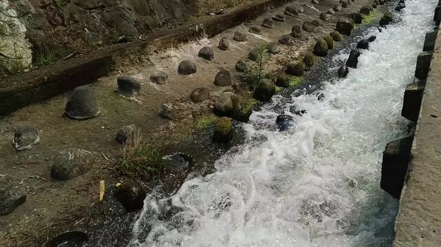Top view of Fresh water streams rapidly through a concrete irrigation canal with stone baffles. For agricultural water management, civil engineering, and environmental conservation concepts