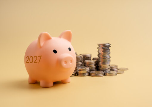 Piggy bank marked 2027 stands beside increasing stacks of coins. Annual savings goals, personal finance planning, money growth. new year budget, and preparation for future financial security concept.