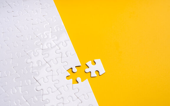 Incomplete white jigsaw puzzle with a detached piece on bright yellow background. Critical missing element, strategic gap, business challenge, integration, and finding the right solution concept.