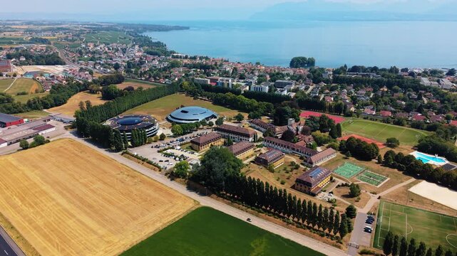 School campus buildings sit beside tennis courts near Lake Geneva, drone pans while pulling back
