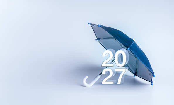 Blue umbrella shelters 2027 numbers on clean background with copy space. Risk protection, business continuity, financial security, contingency planning and preparedness for future uncertainty concept.