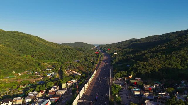 Aerial parallax over Gyeongbu Expressway in Seocho gu, Seoul, South Korea, with vehicles running through a green valley past roadside villas, shops and greenhouses