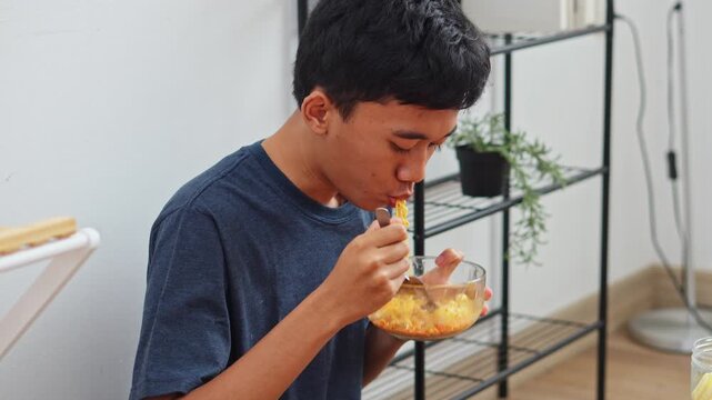 Side view of young Asian male eating noodles and sipping tasty broth at mealtime