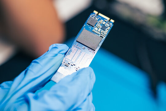 young female tech genius electronics engineer look at solid state drive M.2 NVMe SSD card as conceptual backdrop for computer hardware technology innovation quality control and woman in STEM