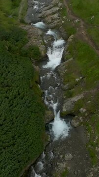 Drone view flying above a rocky river channel with green tundra slopes and eroded banks in the Vachkazhets mountain range, Kamchatka Krai, Russia