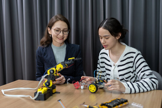 Happy woman student enjoying robotics engineering education learning technology class project building machine together with mentor