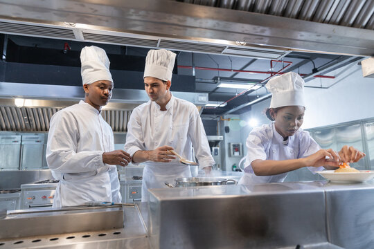 professional chef team working in commercial kitchen man and woman wearing white uniform hat cooking food with serious expression