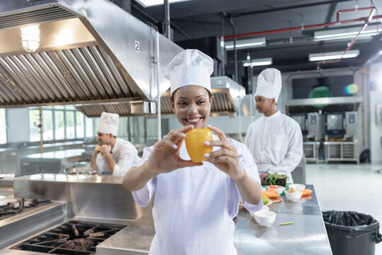 Happy female chef holding yellow pepper commercial kitchen wearing clean uniform smiling with cheerful positive emotion during food preparation