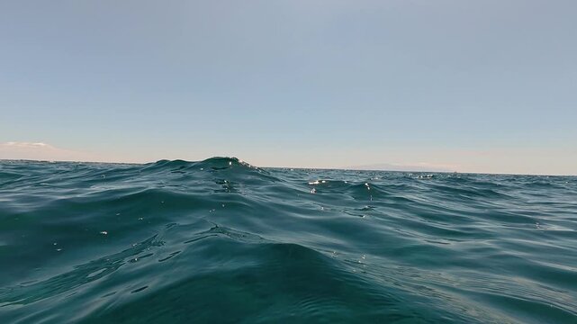Deep blue sea water surface moving with gentle waves creating a mesmerizing and relaxing background, showing a beautiful seascape with the clear sky and horizon line on a sunny summer day