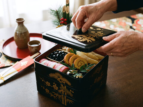 Hands opening a lacquer jubako box filled with Japanese New Year osechi food.