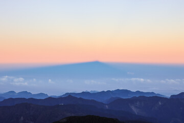 Fototapeta premium Majestic mountain shadow projection over sea of clouds during sunrise, layered alpine landscape