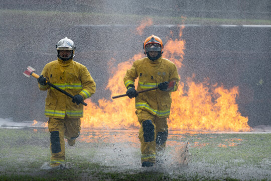 Team of firefighter in fireproof clothe is holding axe to destroy barricade in the burning building with high flame for fire extinguish risk rescue mission and accident management usage