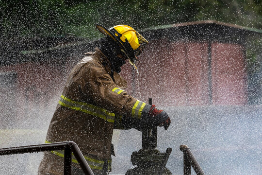Firefighter in fireproof cloth opening water valve near burning building with high flame for fire extinguish risk rescue mission and accident management