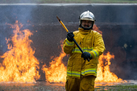 Firefighter in fireproof clothe is holding axe to destroy barricade in the burning building with high flame for fire extinguish risk rescue mission and accident management usage