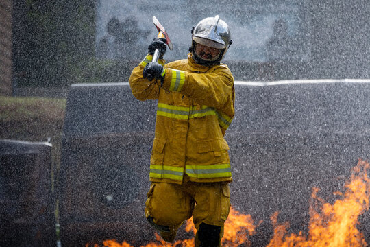 Firefighter in fireproof clothe is holding axe to destroy barricade in the burning building with high flame for fire extinguish risk rescue mission and accident management usage