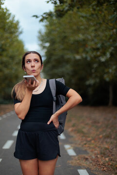 Puzzled Woman Holding Smartphone Sending Voice Message On Forest Pathway. Person using her phone to send voice message outdoors
