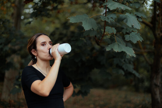 Thirsty Woman Drinking From Reusable Bottle in a Forest. Female explorer drinks water from reusable bottle while resting in nature