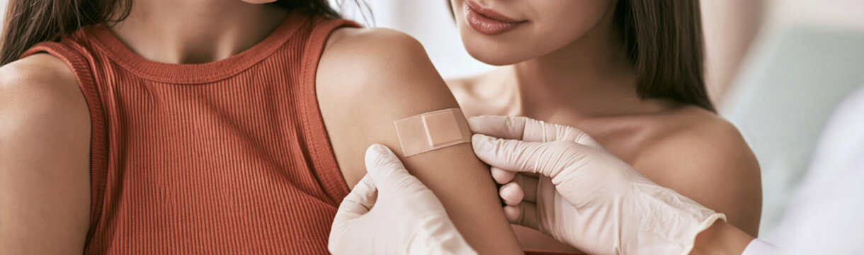 Getting a Bandage: A close-up shot shows a gloved hand applying a bandage to a young person's arm after an injection, emphasizing care and recovery.