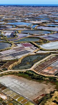 Panning aerial view over colorful Guerande salt marshes with salt evaporation ponds, winding dikes and Atlantic ocean on horizon near Plage des Oceanides France