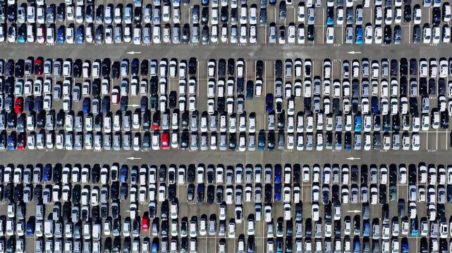 Full frame top down view of thousands of new cars parked in dense rows at Port of Bordeaux vehicle lot in France forming geometric pattern with lane arrows